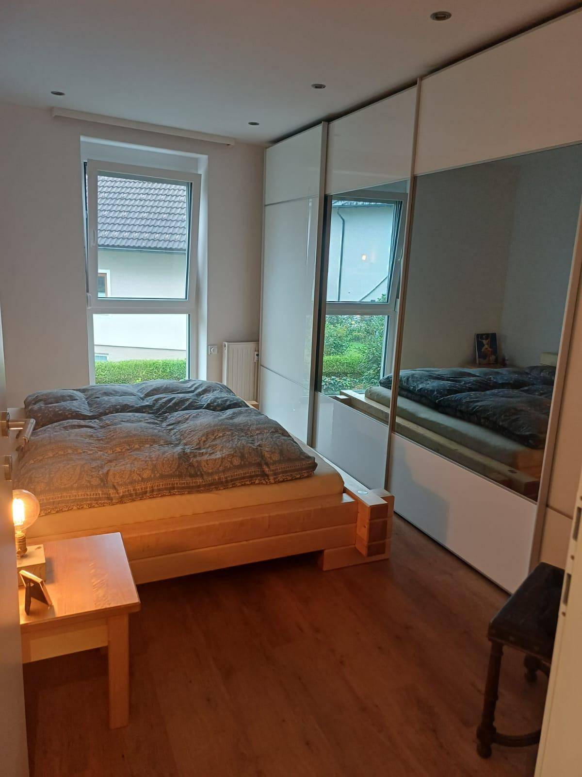 Helles Schlafzimmer mit Holzbett, zwei Fenstern und modernen Einbauschränken.