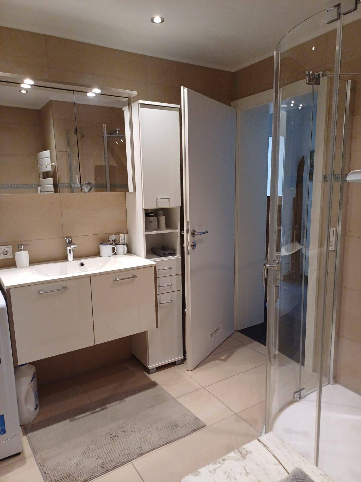 Funktionales Badezimmer mit Einzelwaschbecken, Spiegelschrank und Duschkabine.