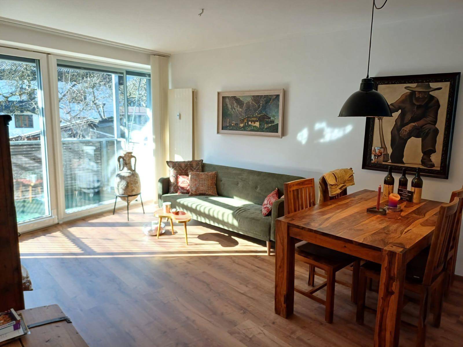 Offener Wohn-Essbereich mit grünem Sofa, Holztisch und viel natürlichem Licht.