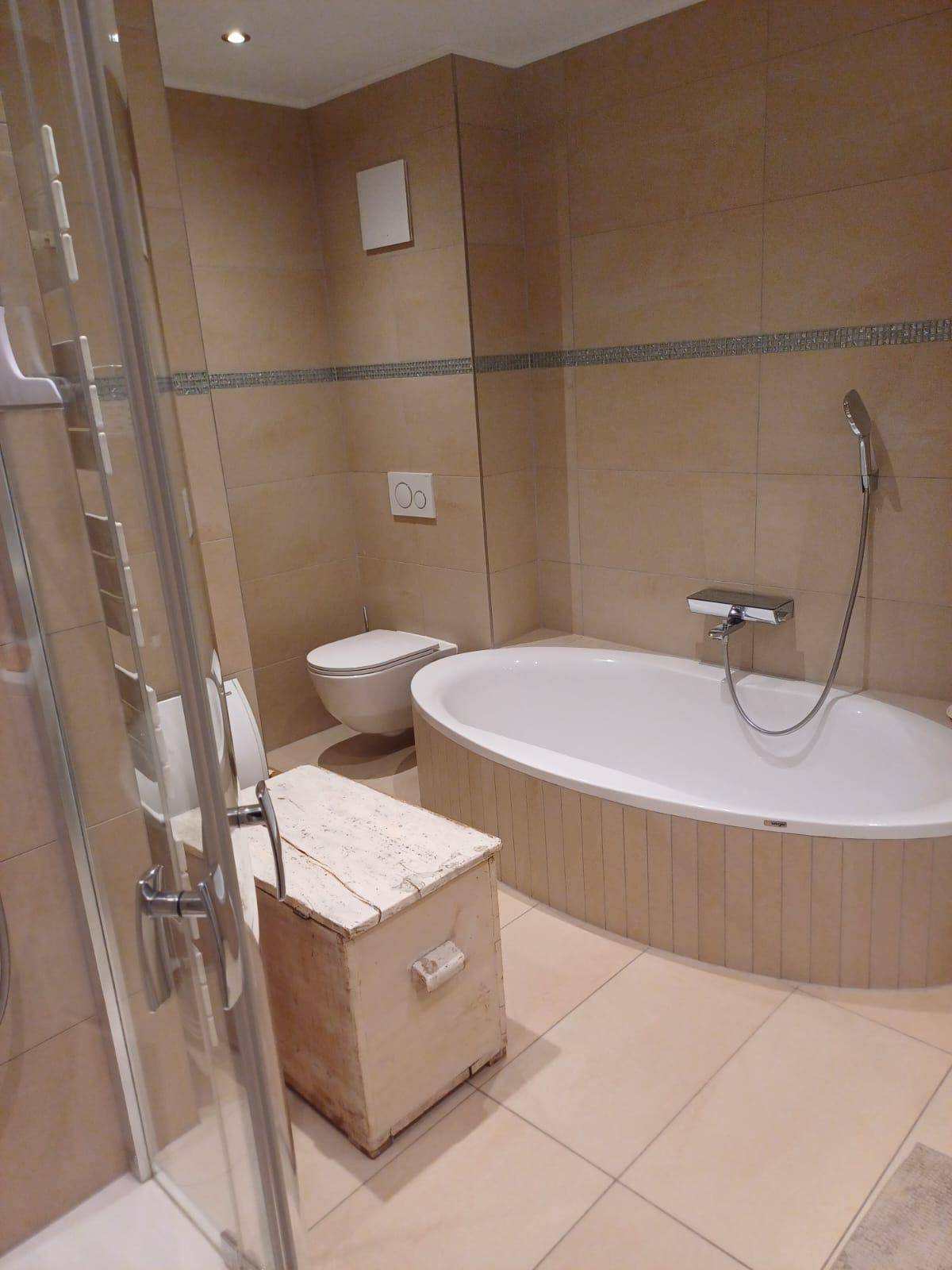 Helles Badezimmer mit beigen Fliesen, Badewanne, Duschkabine und Wand-WC.