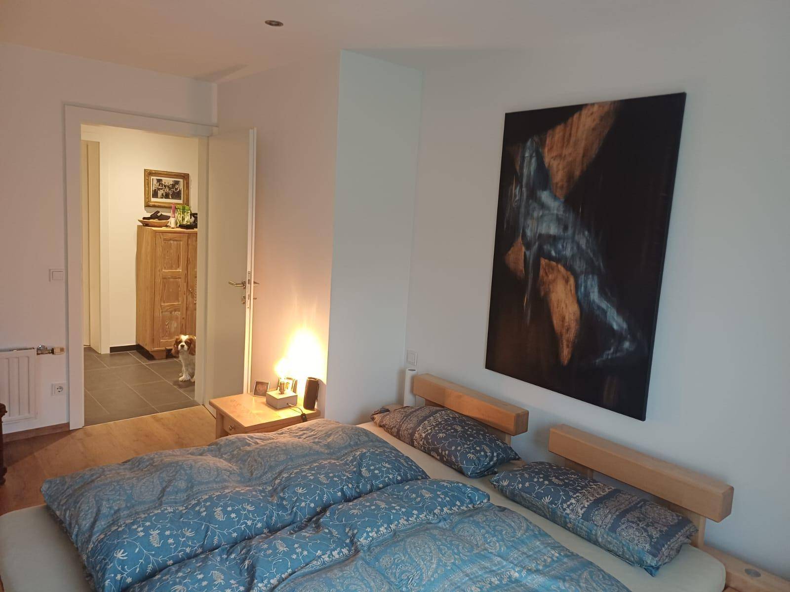 Schlafzimmer mit Holzbett, blauer Bettwäsche und einem großen Kunstwerk an der Wand.