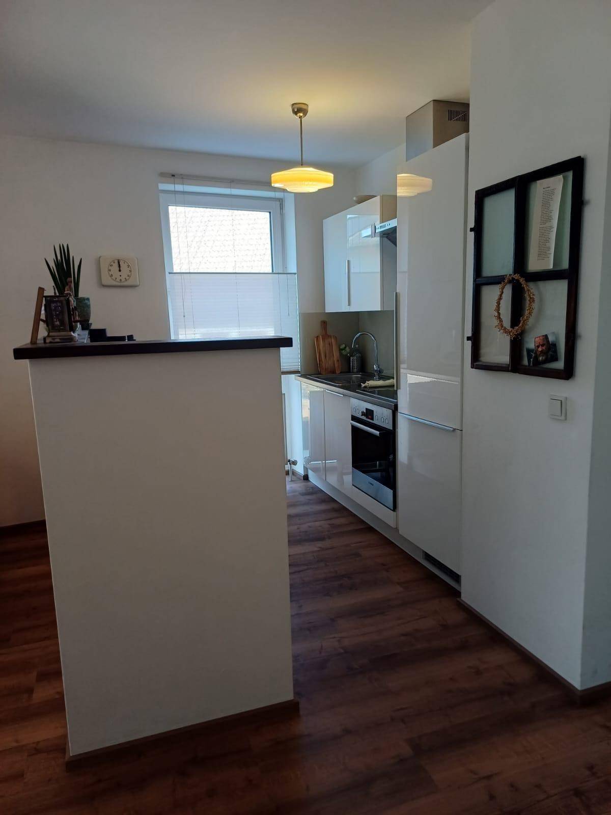 Moderne Küche mit weißen Hochglanzfronten, integrierten Geräten und Frühstücksbar.