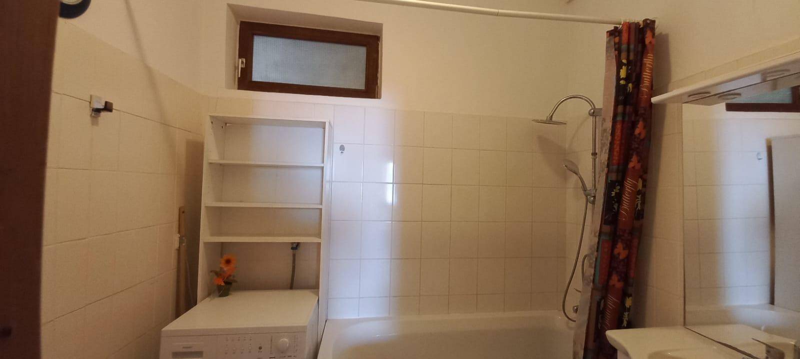 Helles Badezimmer mit Badewanne, Dusche, weißen Fliesen und einem kleinen Fenster.