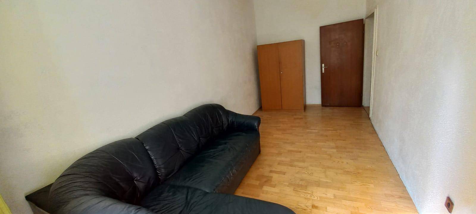 Geräumiges Wohnzimmer mit schwarzem Ledersofa, Holzboden und schlichten, hellen Wänden.