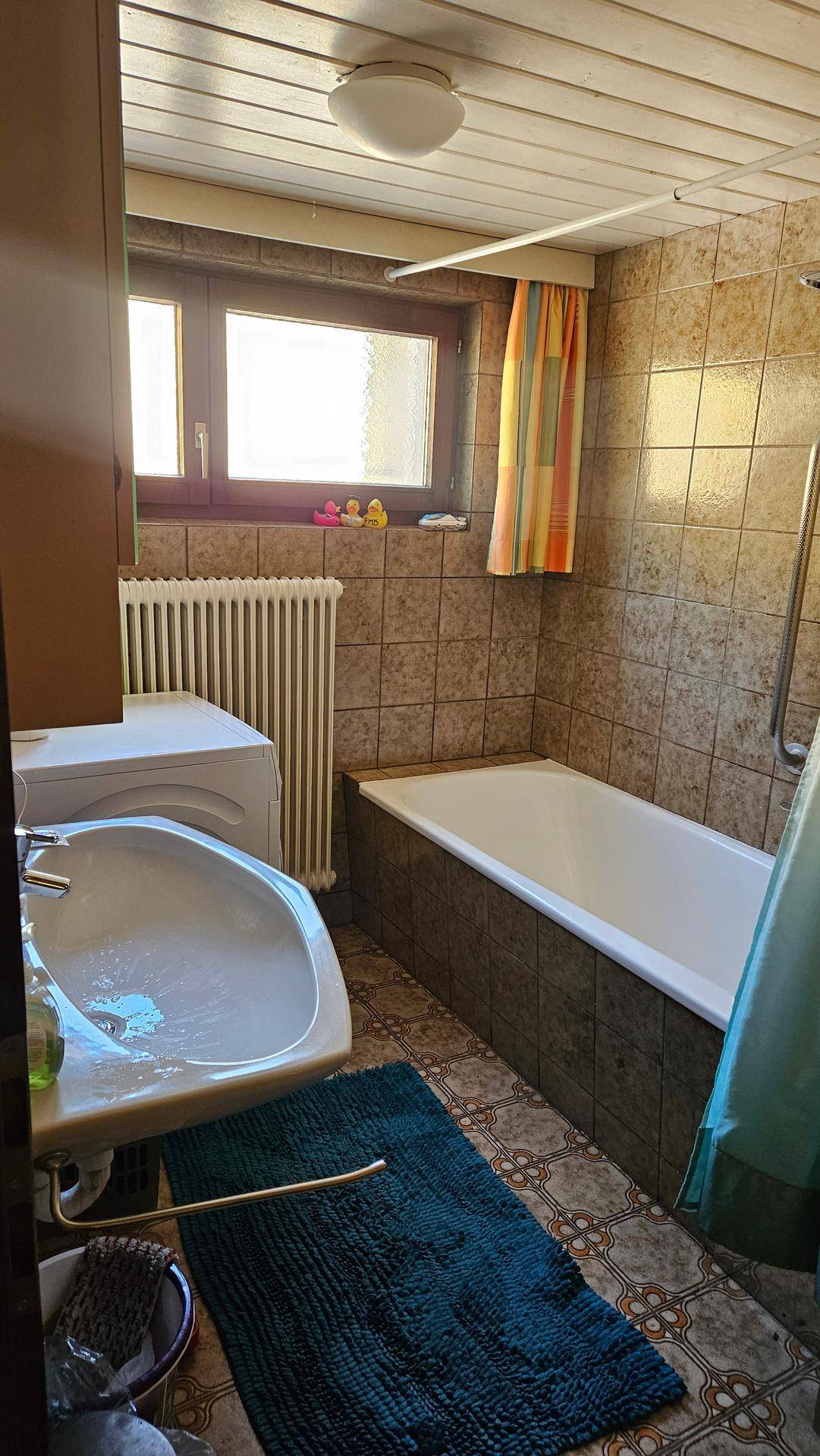 Badezimmer mit Badewanne, Waschbecken, Heizkörper und Fenster für natürliche Belüftung.