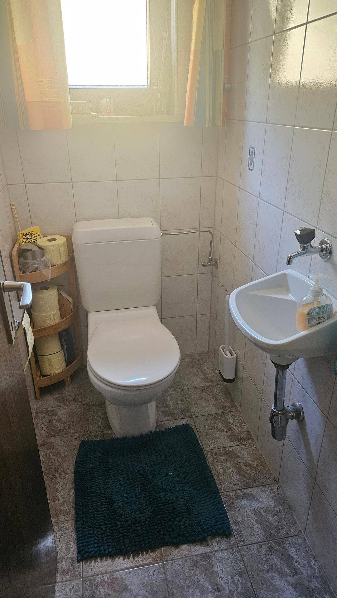 Kleines Gäste-WC mit Fliesen, Toilette, Waschbecken und Fenster für Tageslicht.