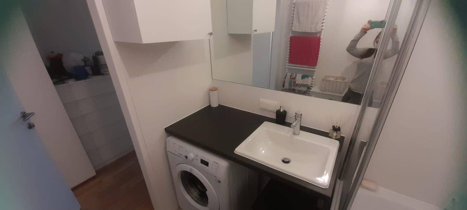 Modernes Badezimmer mit Waschbecken, Spiegel, Duschkabine und integrierter Waschmaschine.