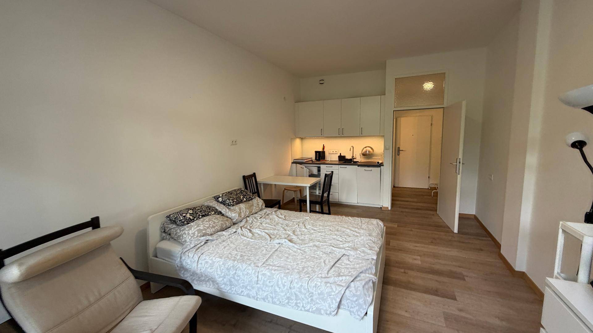 Helles Studiozimmer mit Bett, Holzboden und integrierter Küchenzeile für effizientes Wohnen.