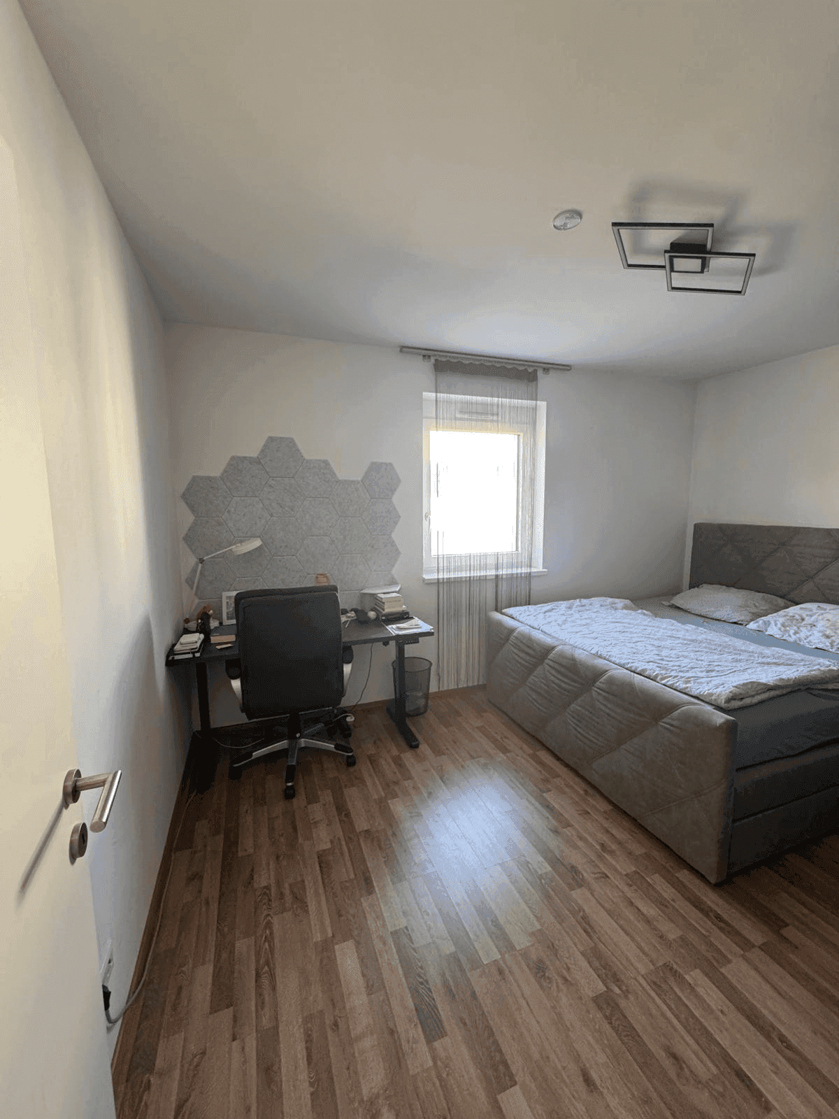 Schlafzimmer mit Doppelbett, Schreibtisch und Fenster für natürliches Licht.