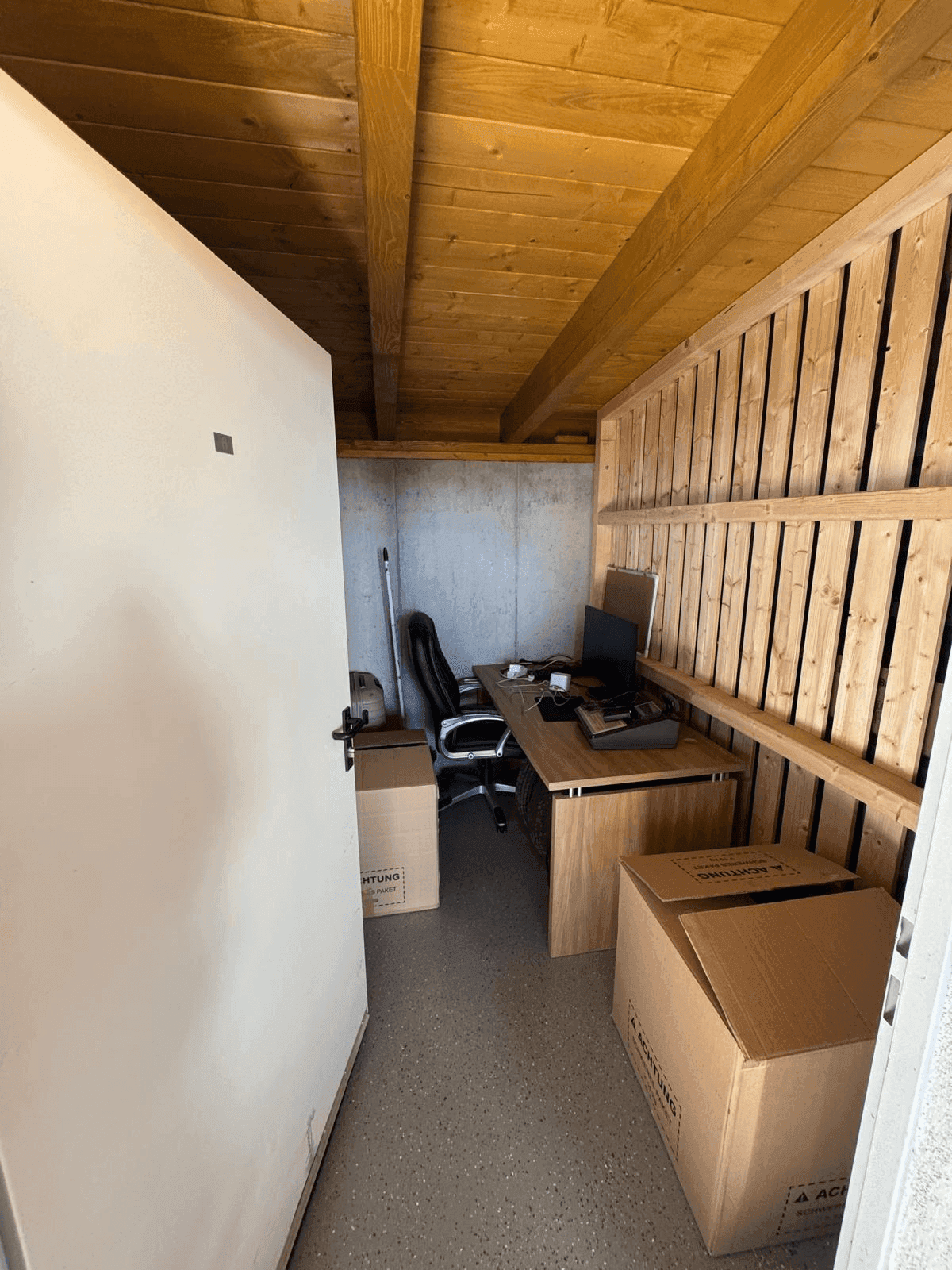Kleiner Arbeitsraum mit Holzbalken, Schreibtisch und Lagerboxen.
