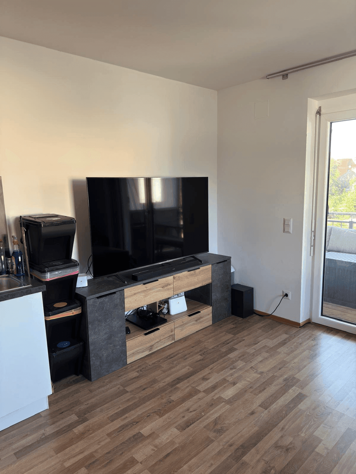 Wohnbereich mit großem Fernseher, Medienmöbeln und Zugang zum Balkon.