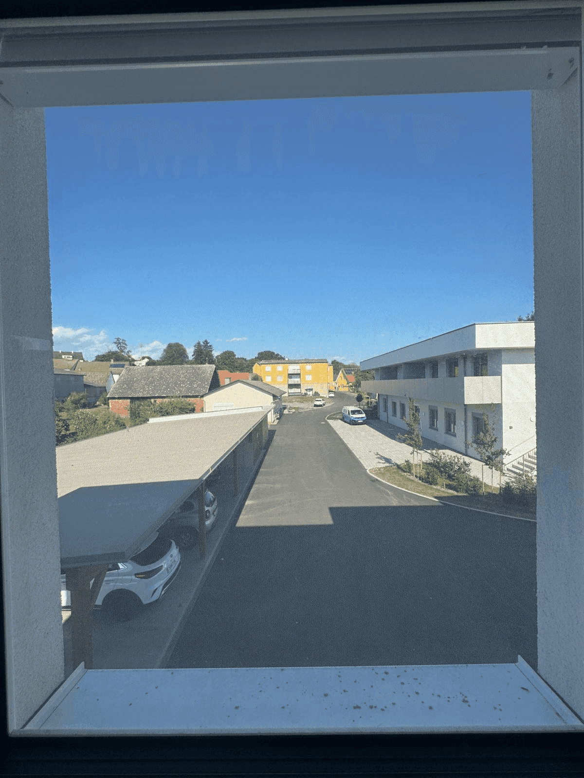 Blick aus dem Fenster auf die Nachbarschaft mit Parkplätzen und Gebäuden.
