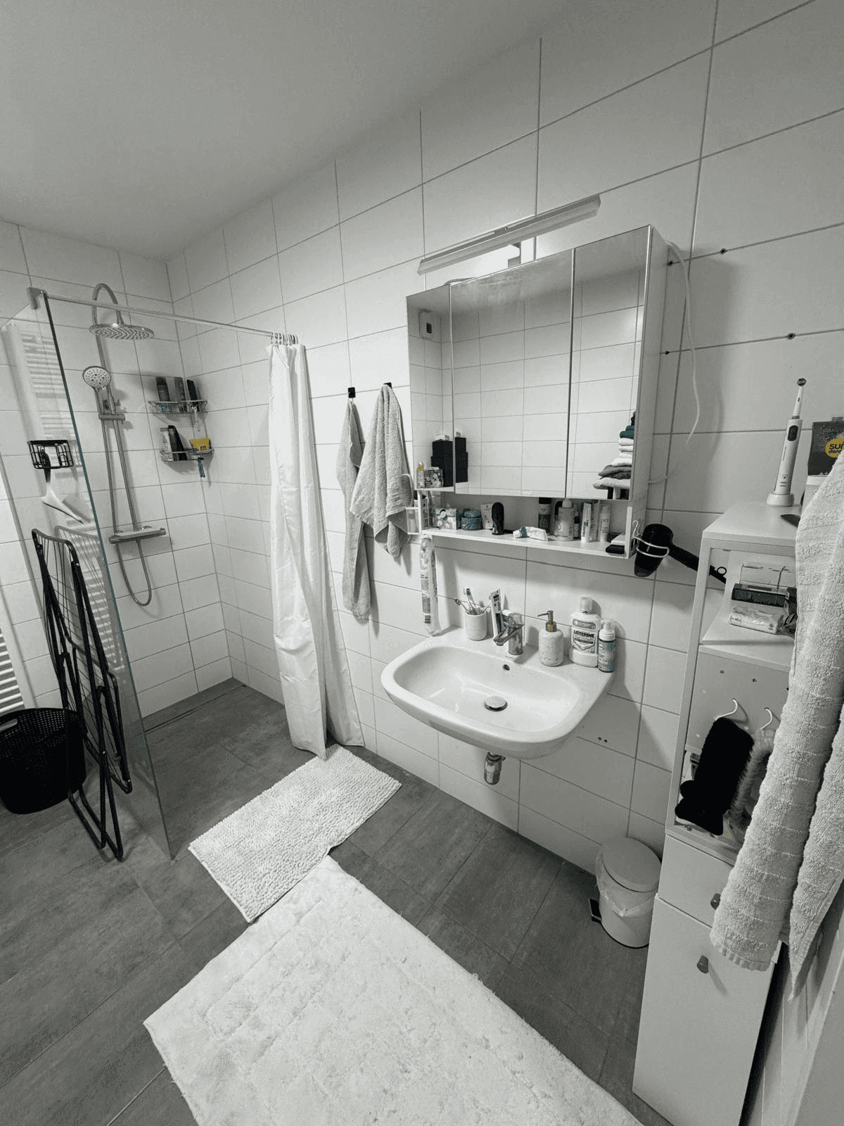 Helles Badezimmer mit weißen Fliesen, Dusche und Waschbecken.