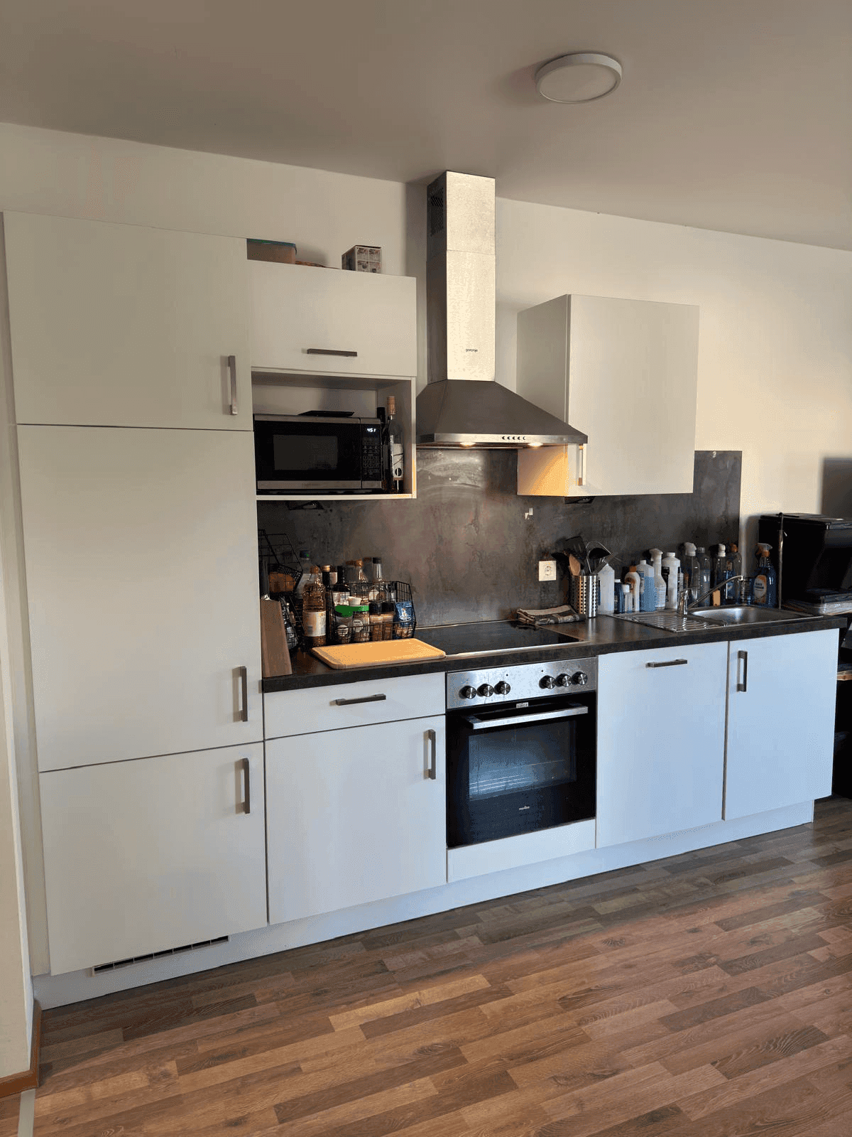 Funktionale Küche mit weißen Schränken, integriertem Backofen und Mikrowelle.