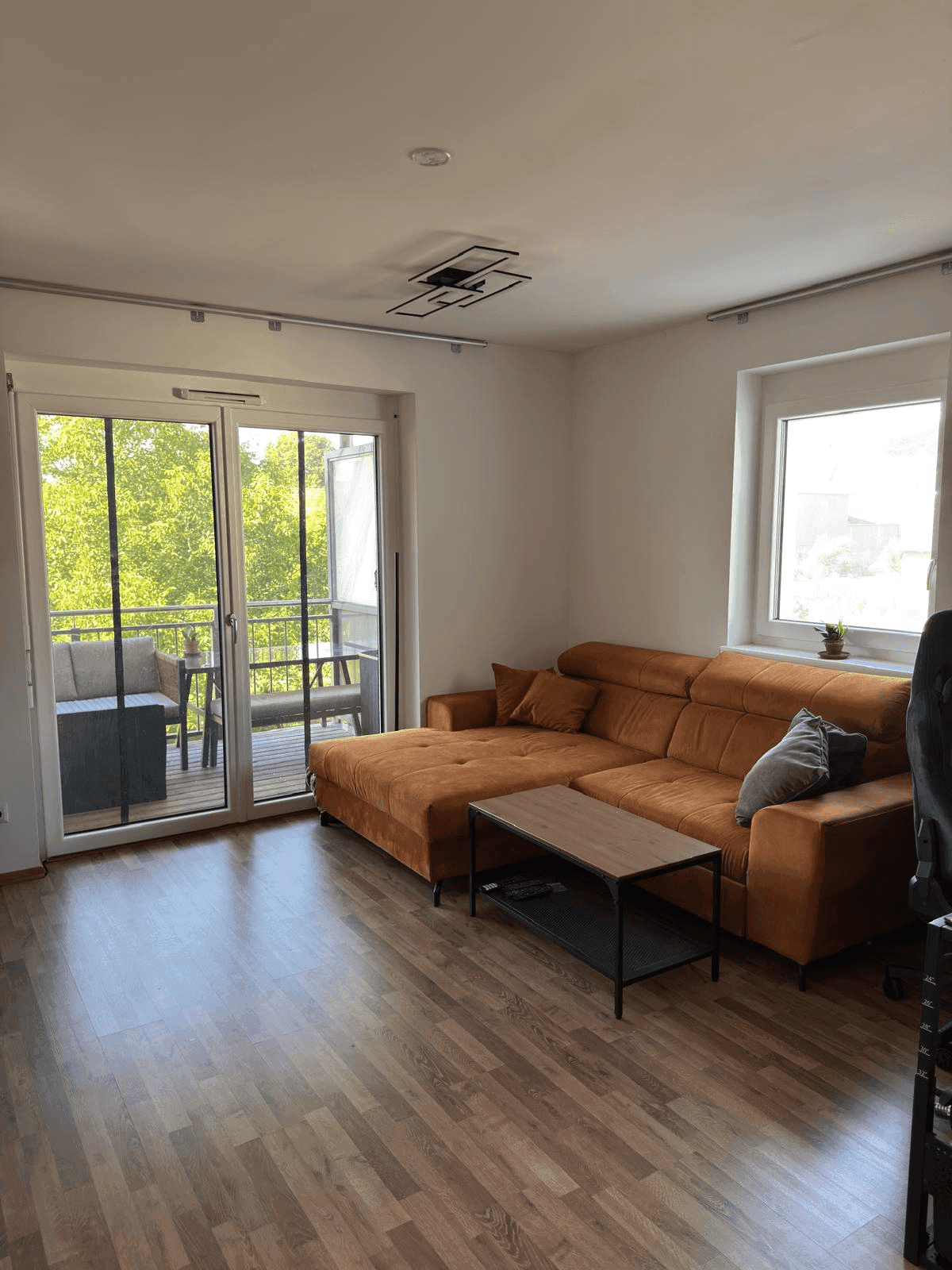 Gemütliches Wohnzimmer mit großem Ecksofa, Holzboden und Zugang zum Balkon.