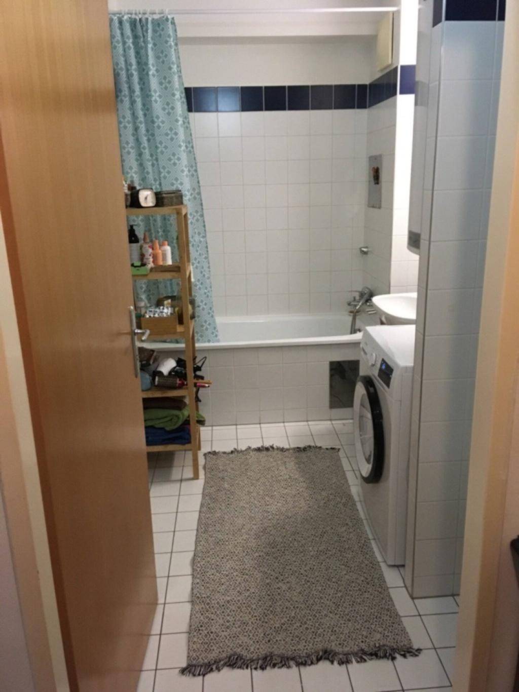 Helles Badezimmer mit Badewanne, Waschmaschine und weißen Fliesen mit einer blauen Akzentlinie.