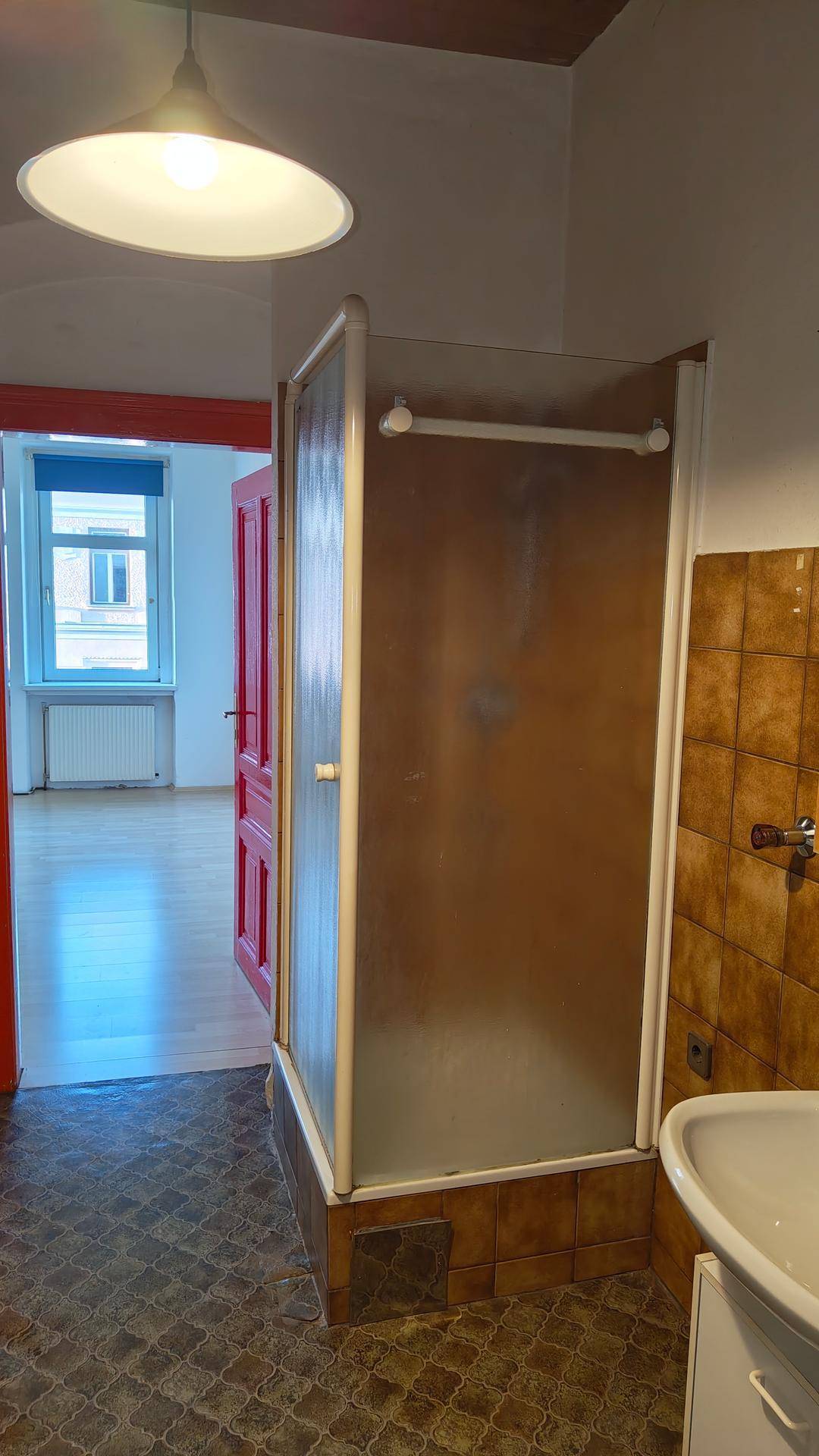 Badezimmer mit Duschkabine, Waschbecken und gemusterten Fliesen, mit Zugang zu einem weiteren Raum.