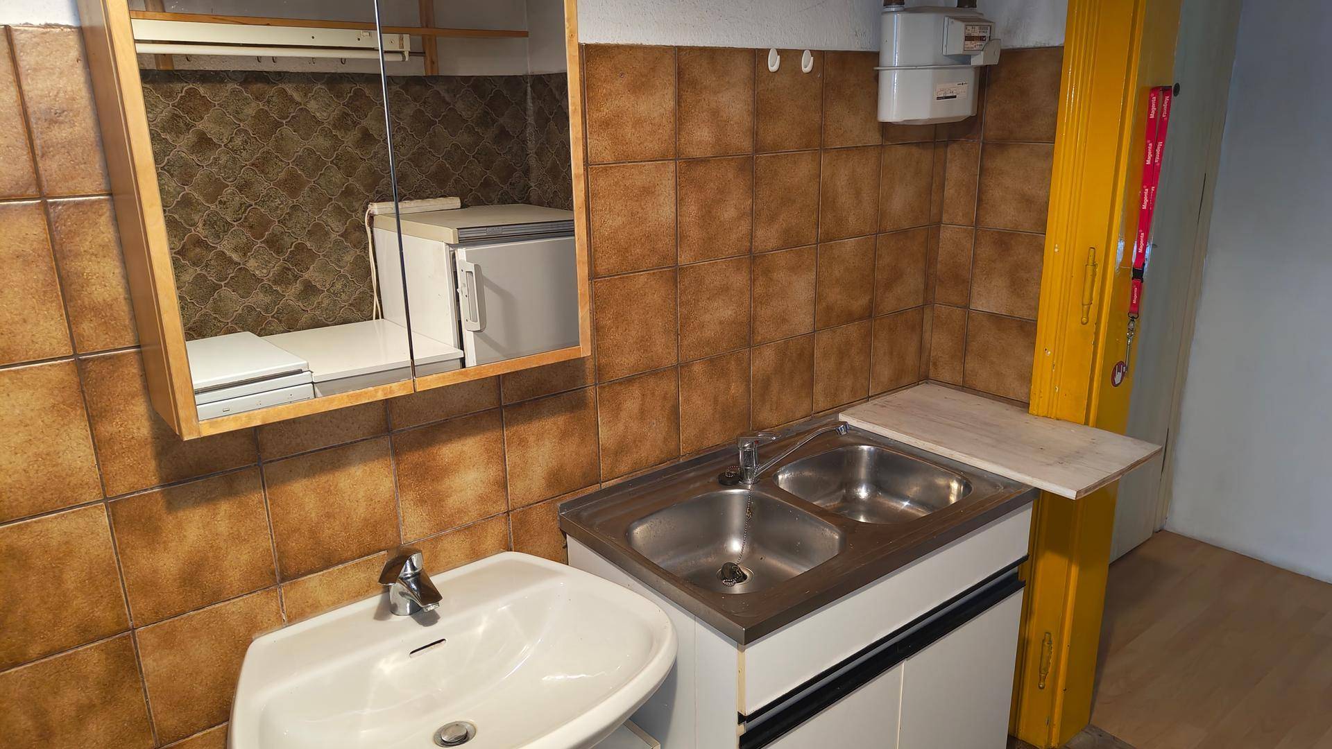 Funktionaler Raum mit braunen Fliesen, Einzelwaschbecken, Doppelspüle und Spiegelschrank.
