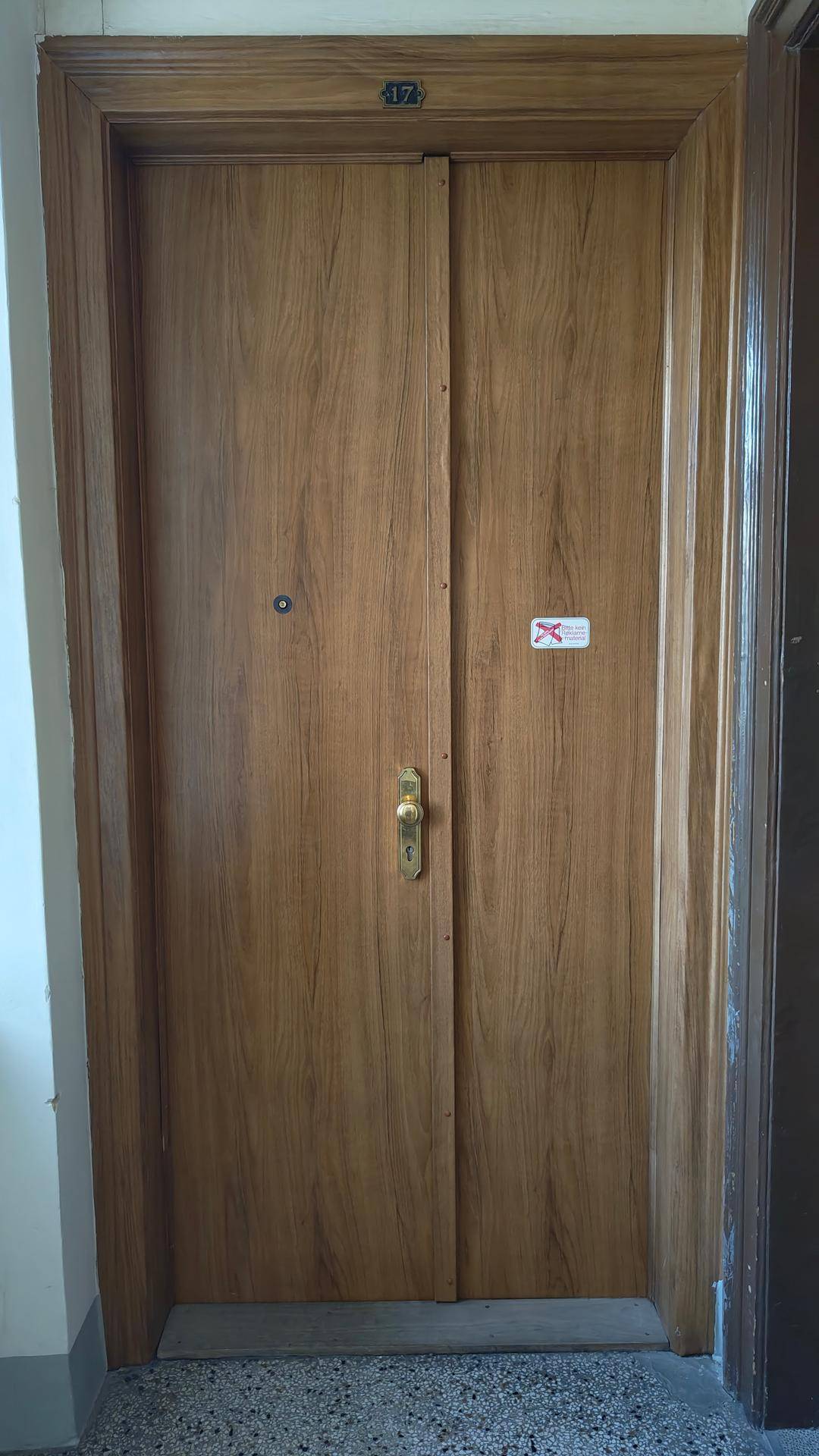 Dunkle Holztür mit Doppelflügeln und goldener Klinke, mit der Nummer 17 darüber im Treppenhaus.
