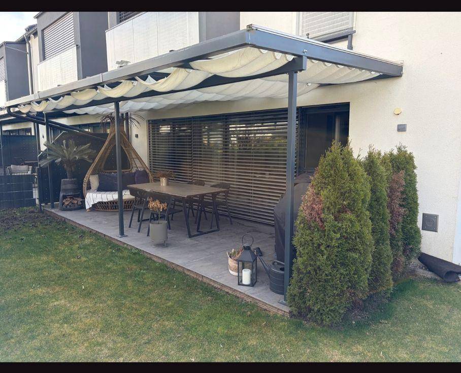 Große Terrasse mit Pergola, Essbereich und Liegemöglichkeiten, umgeben von Grünflächen.
