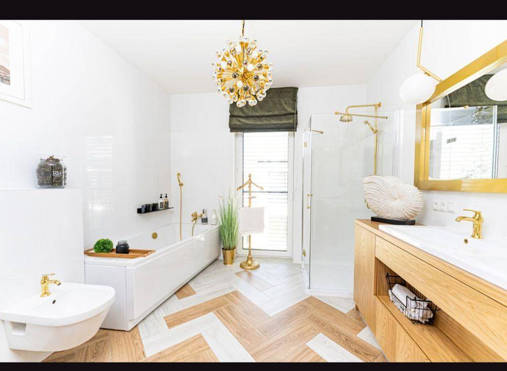 Elegantes Badezimmer mit Badewanne, Dusche, Fenster und hochwertigen Armaturen in Gold.