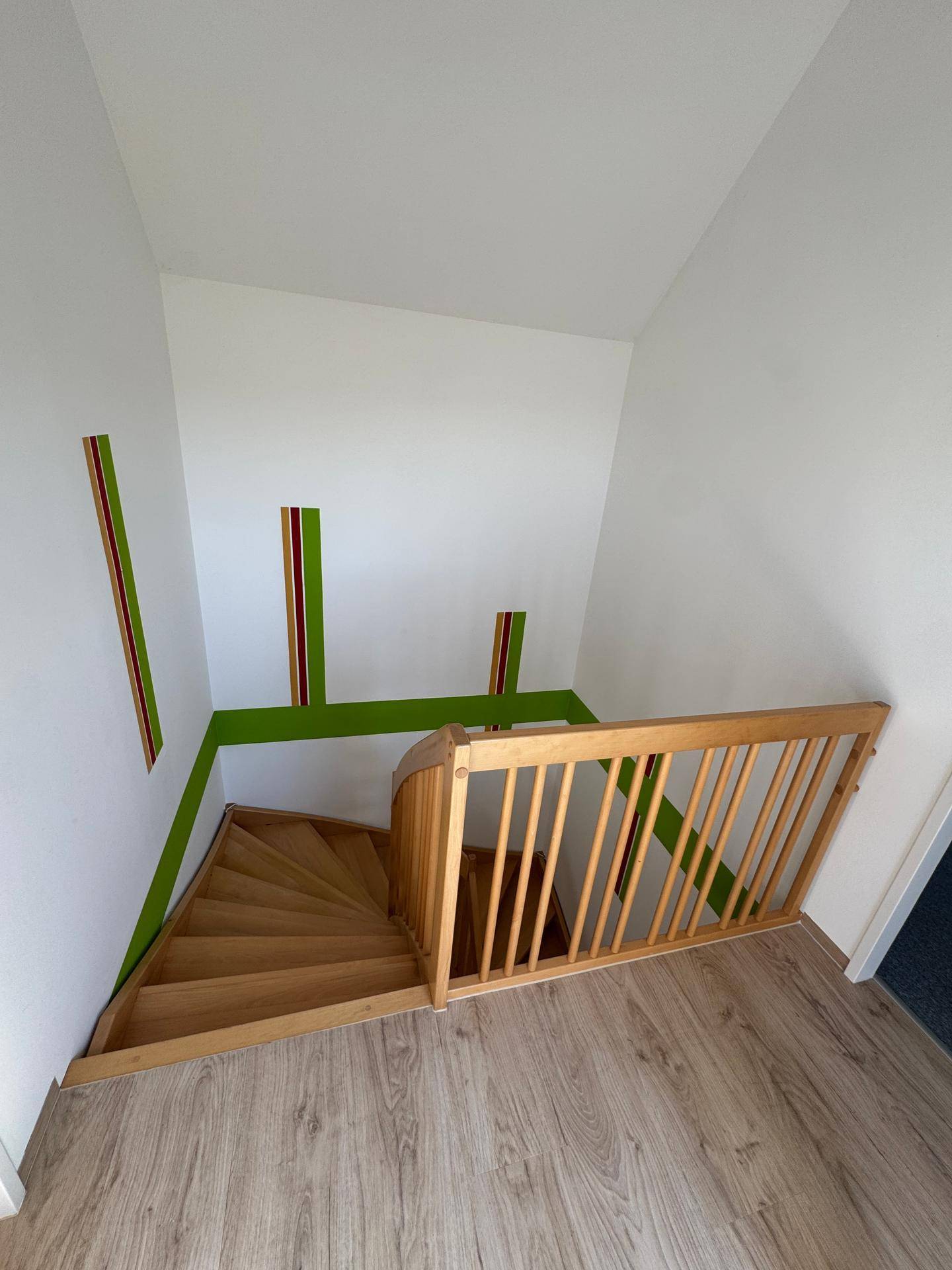Holztreppe mit Kindersicherung und farbigen Akzenten an den Wänden im Treppenhaus.