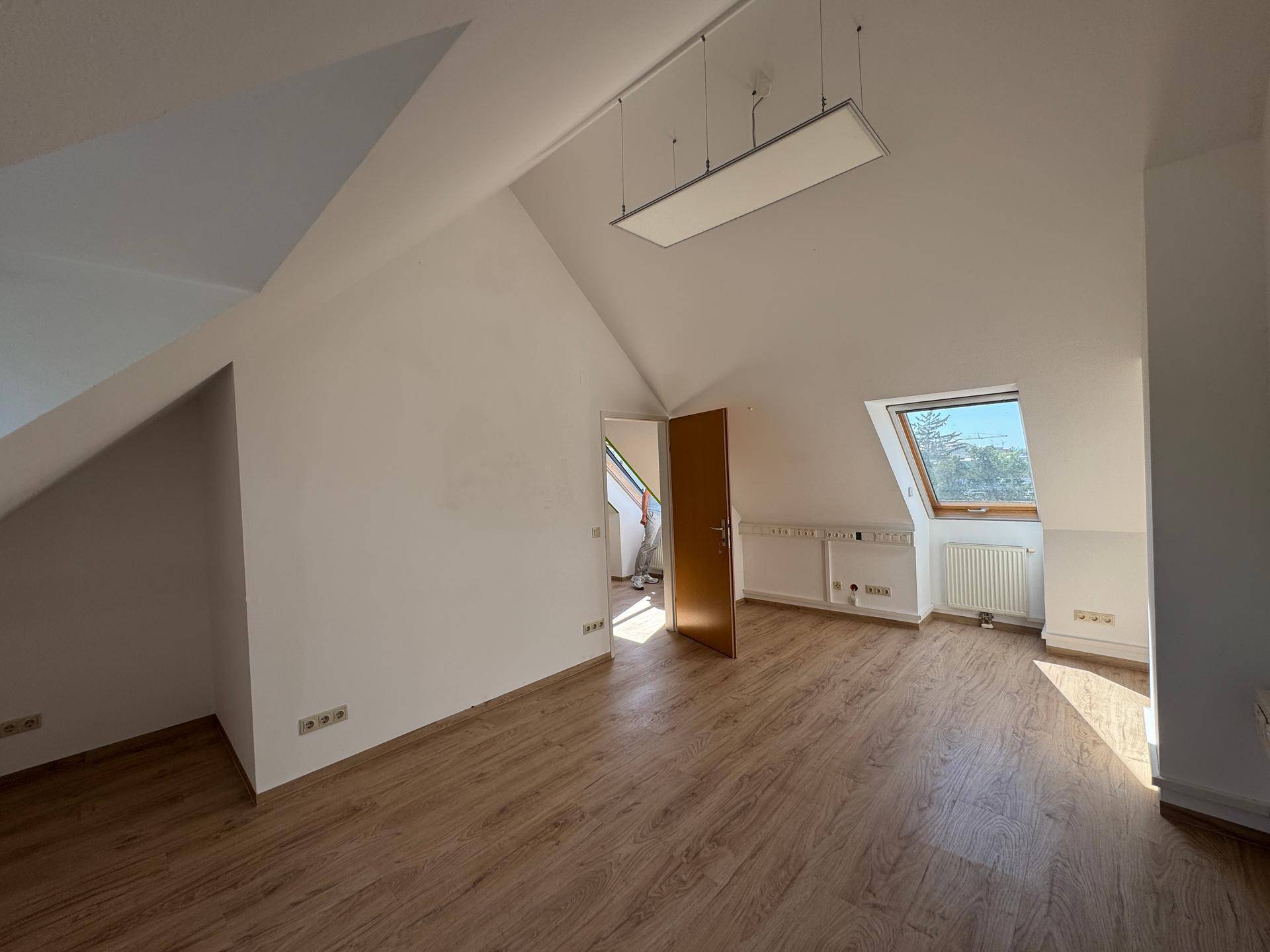 Helles Zimmer mit Laminatboden, Dachschrägen und einem Dachfenster, das viel Licht hereinlässt.