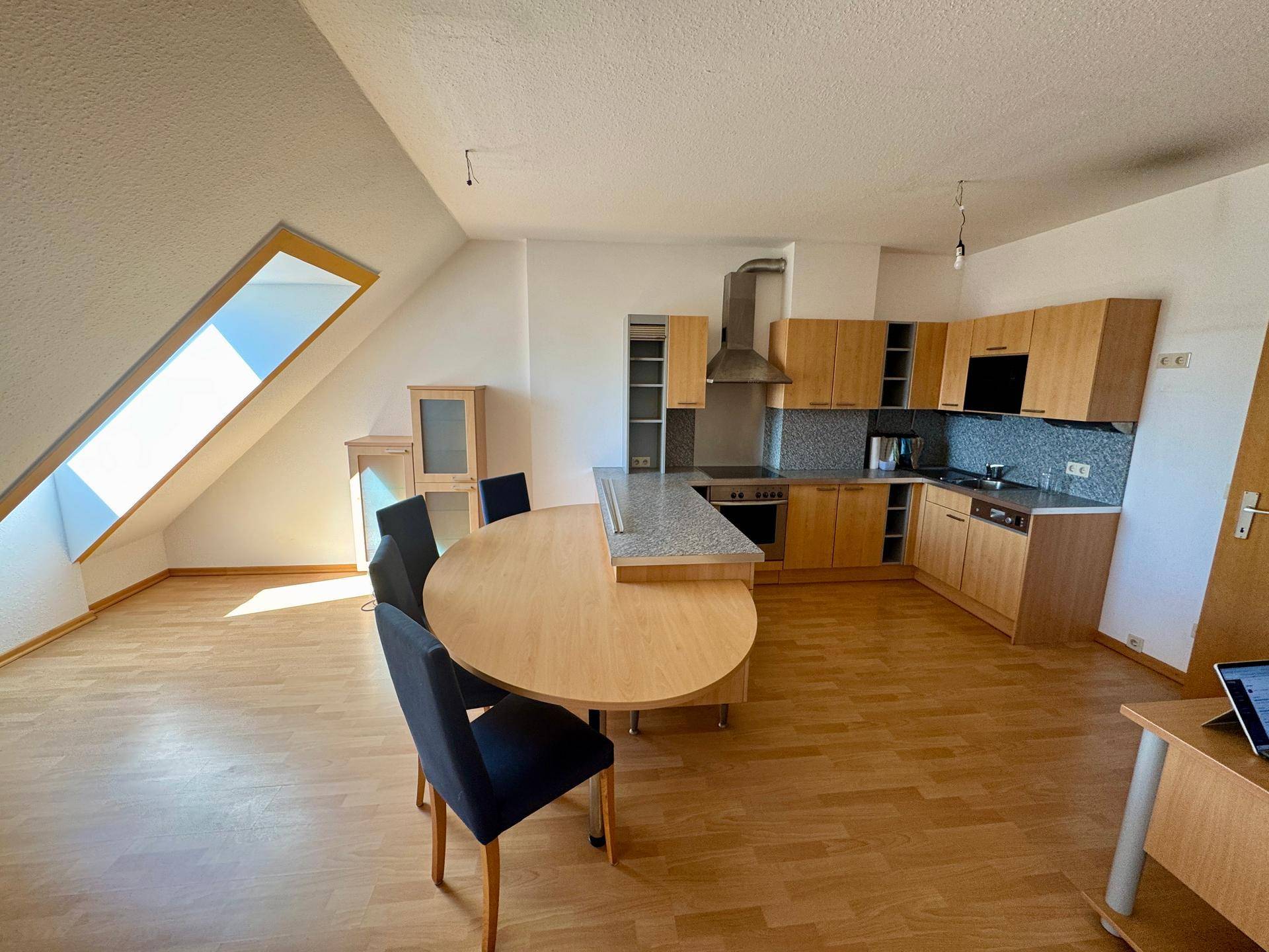 Offene Wohnküche mit Holzelementen, Essbereich und viel Tageslicht durch das Dachfenster.