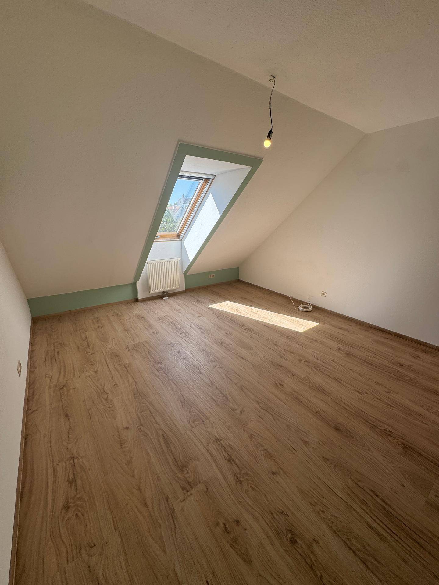 Lichtdurchflutetes Zimmer mit Laminatboden, Dachschräge und einem großen Dachfenster.