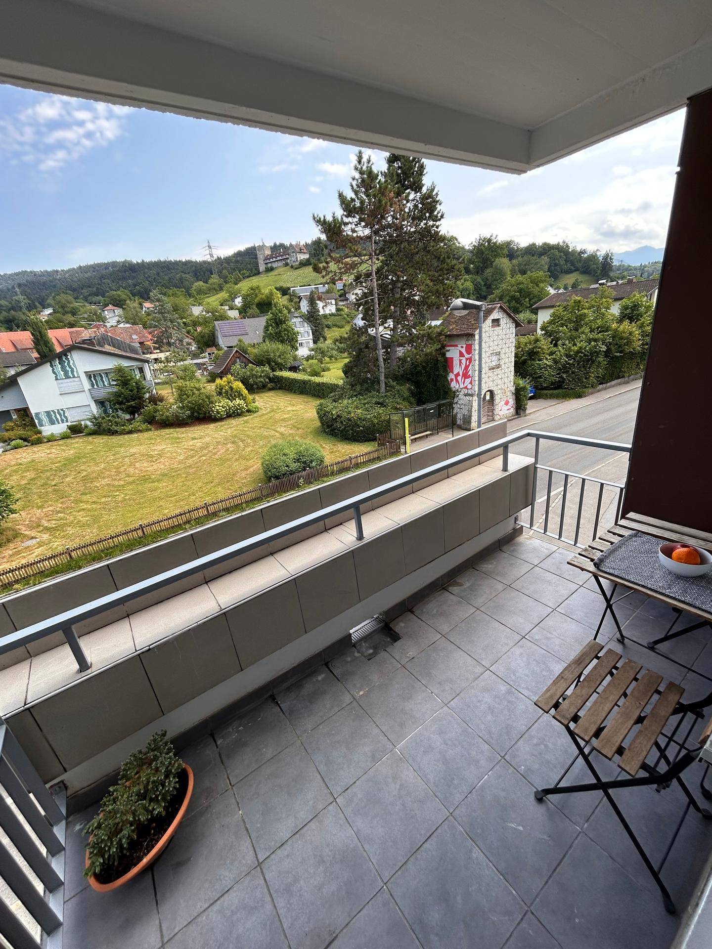 Balkon mit Sitzgelegenheiten und weitem Blick über die grüne Landschaft und umliegende Häuser.