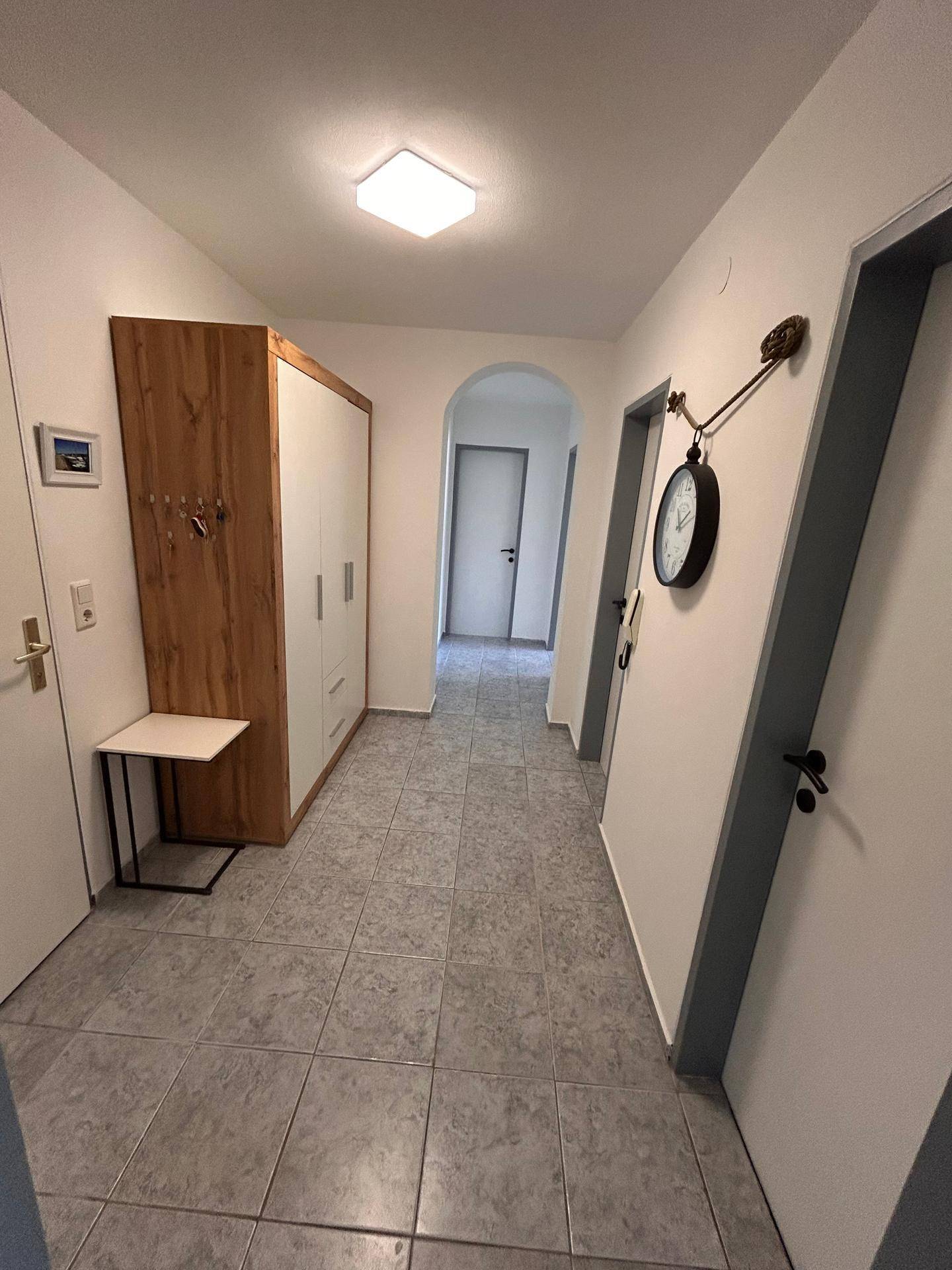 Heller Flur mit Fliesenboden und Garderobe, der zu verschiedenen Zimmern führt.