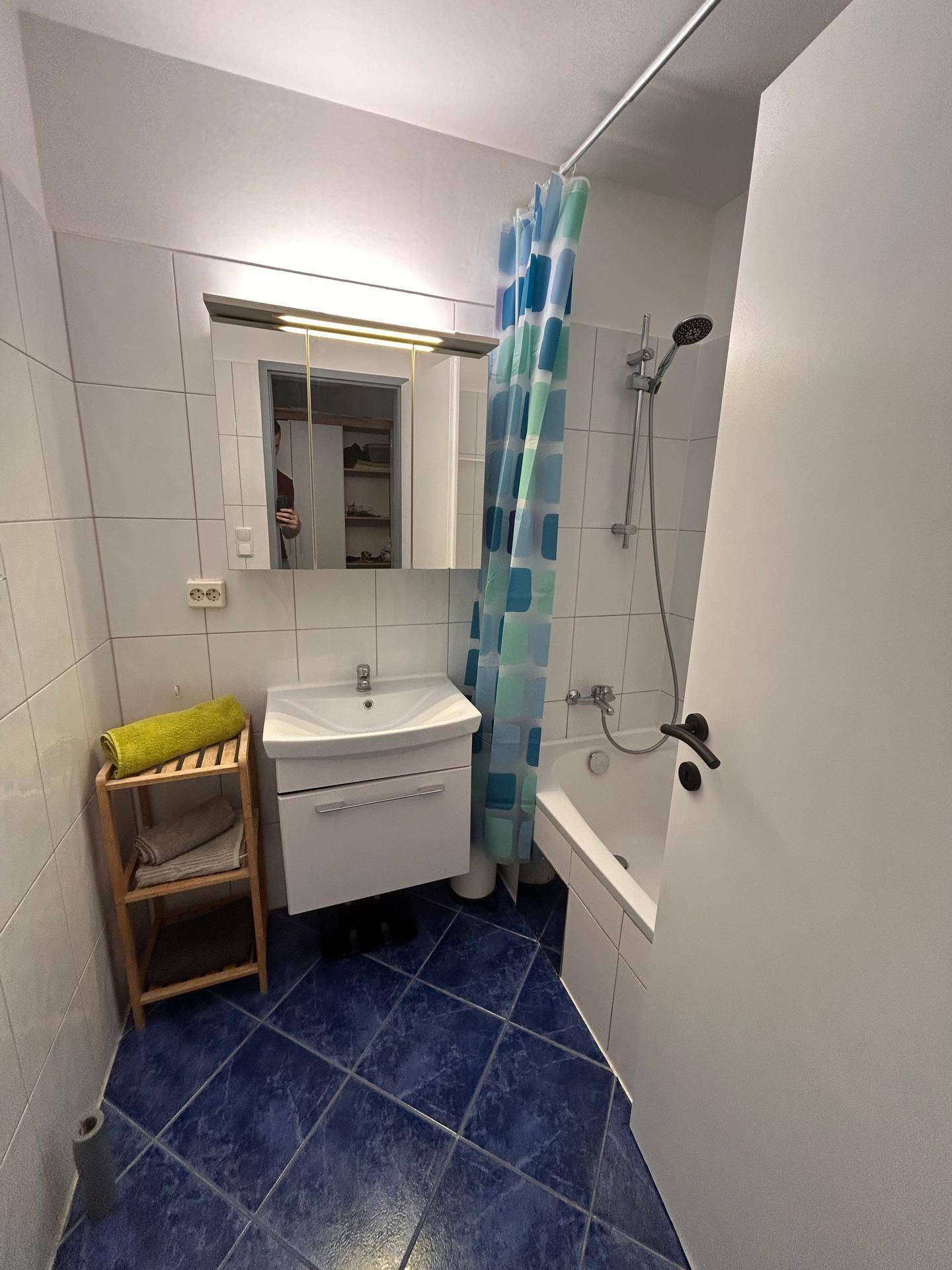 Badezimmer mit Badewanne, Waschbecken und Spiegelschrank, ausgestattet mit blauen Bodenfliesen.