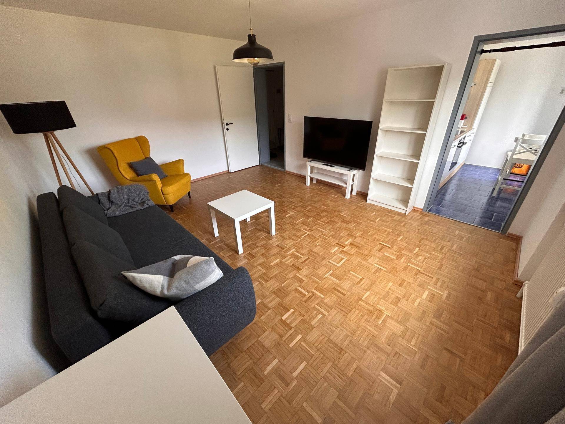 Geräumiges Wohnzimmer mit Parkettboden, TV-Bereich und Zugang zu weiteren Räumen.
