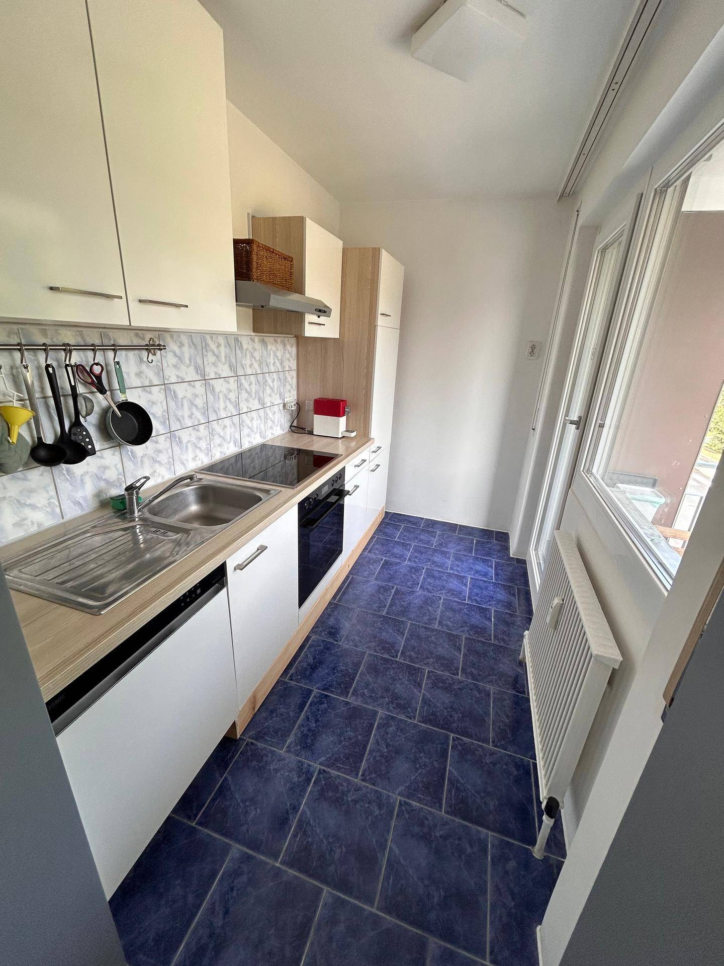 Funktionale Küche mit weißen Schränken, Holz-Arbeitsplatte und blauen Fliesen, mit Zugang nach draußen.