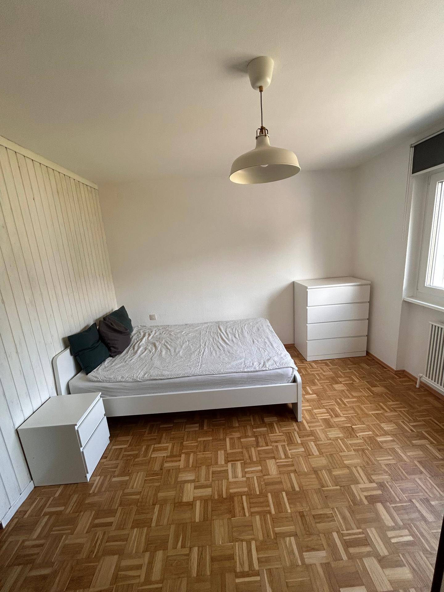 Schlafzimmer mit Doppelbett, Kommode und Parkettboden, bietet eine helle und ruhige Atmosphäre.