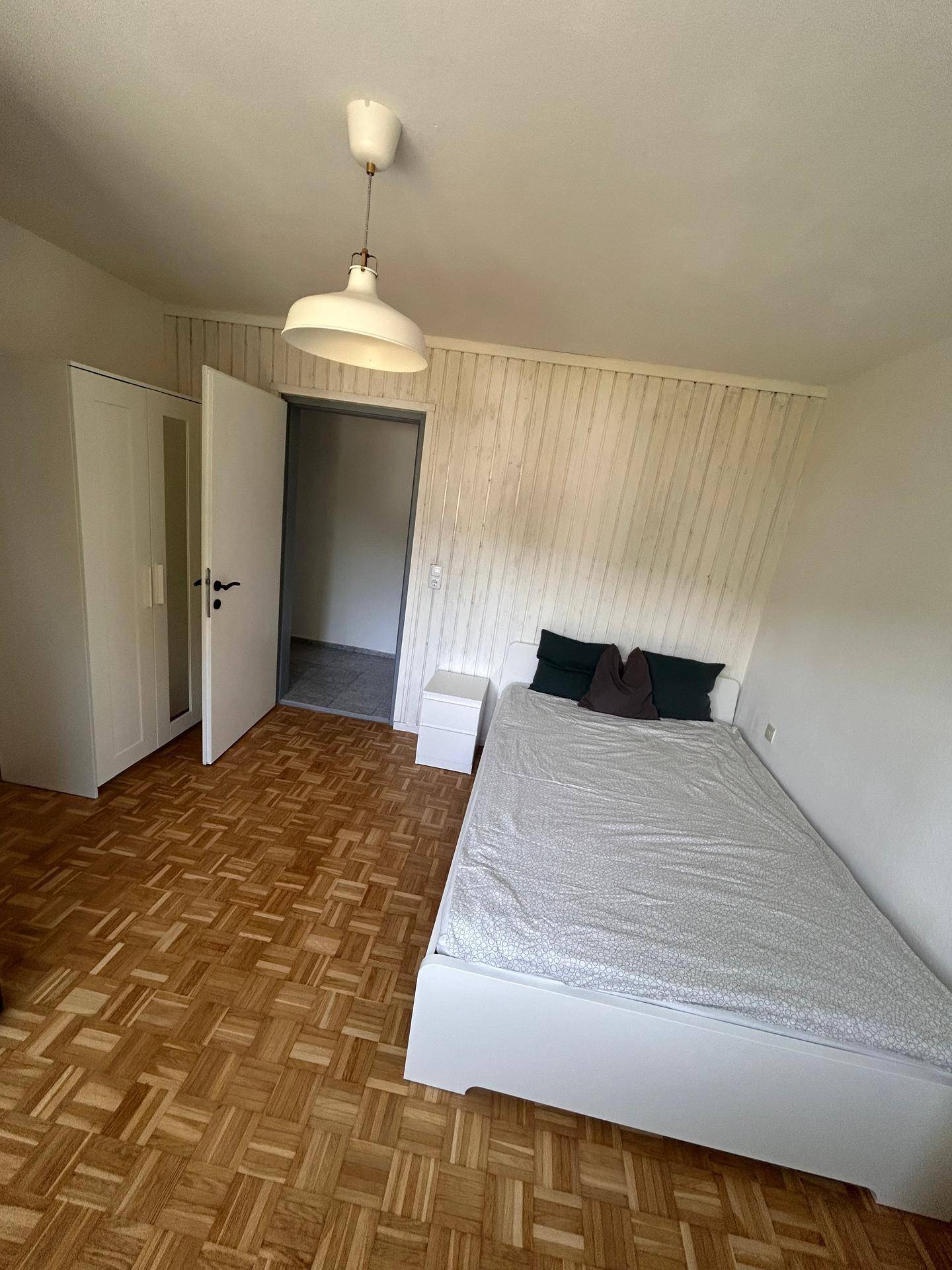 Helles Schlafzimmer mit Parkettboden, Kleiderschrank und Zugang zu einem weiteren Raum.