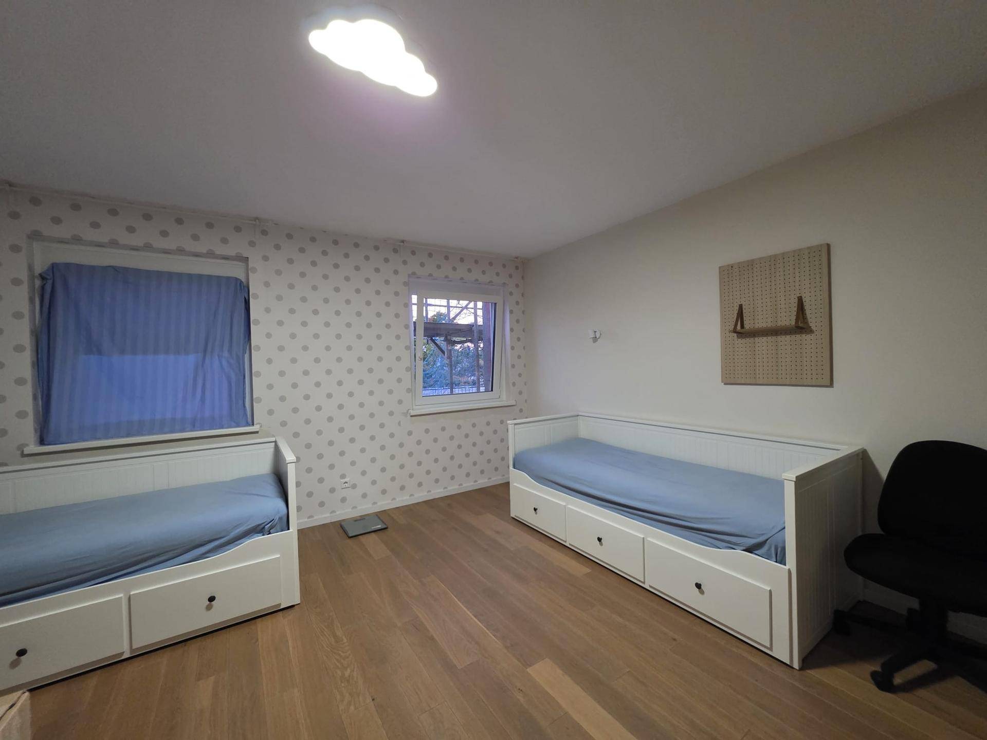 Helles Kinderzimmer mit zwei Betten, Holzfußboden und verspielter Punkt-Tapete.
