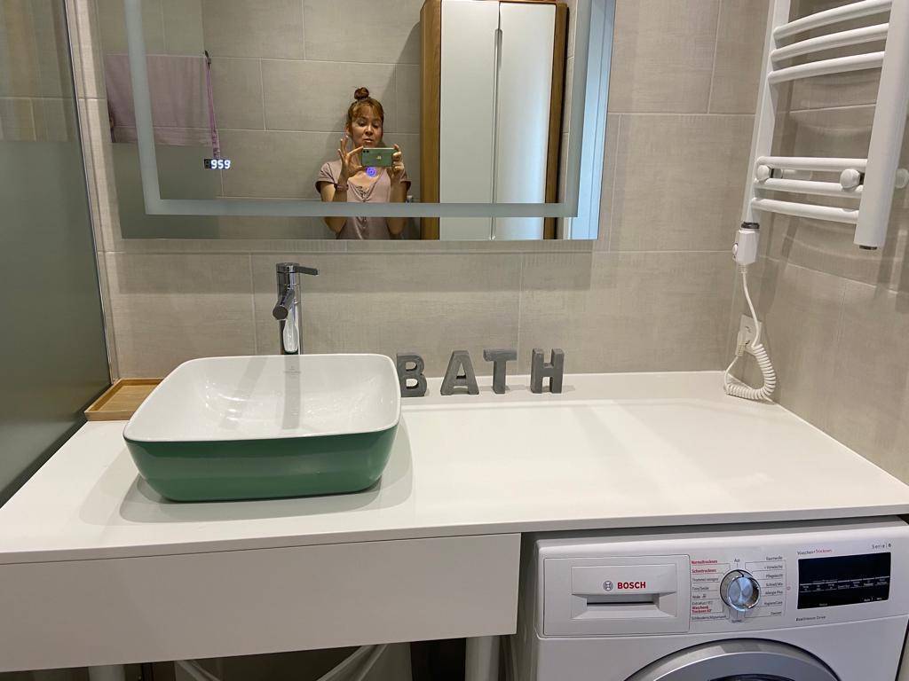 Modernes Badezimmer mit Waschmaschine, Aufsatzwaschbecken und beleuchtetem Spiegelschrank.