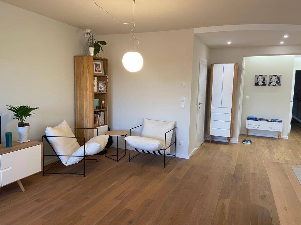 Gemütlicher Wohnbereich mit modernen Sesseln, Holzregal und hellem Holzfußboden.