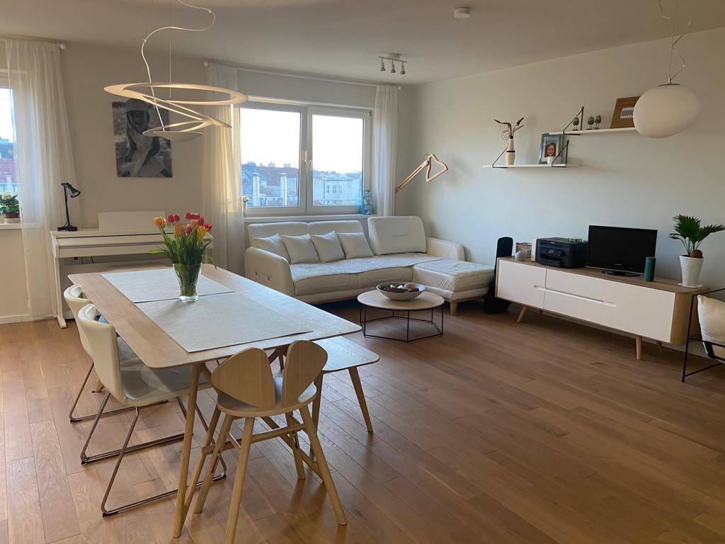 Heller Wohn- und Essbereich mit Sofa, Esstisch und großen Fenstern, die viel Licht hereinlassen.