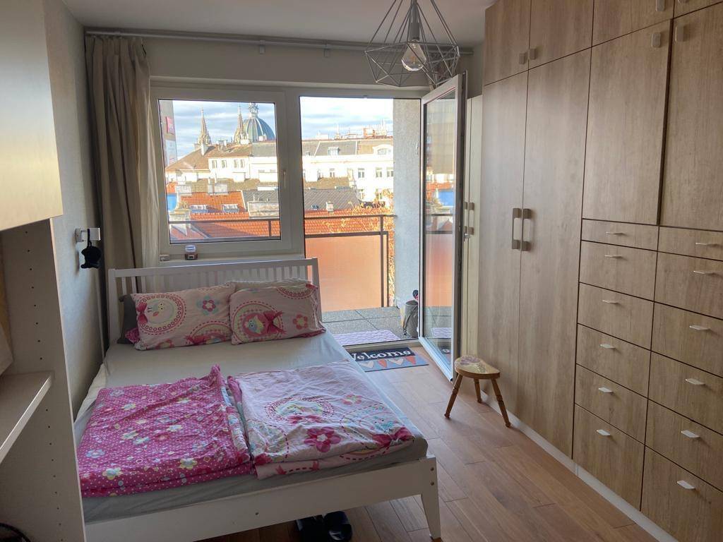 Schlafzimmer mit Holzboden, Einbauschränken und Zugang zu einem Balkon mit Stadtblick.