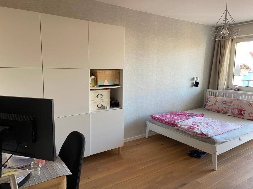 Helles Schlafzimmer mit Holzboden, weißem Bett und Schrank, sowie einem Arbeitsbereich.
