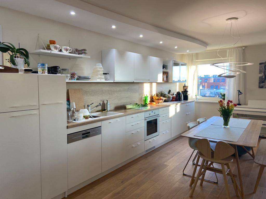 Moderne weiße Einbauküche mit Essbereich, integrierten Geräten und Blick nach draußen.