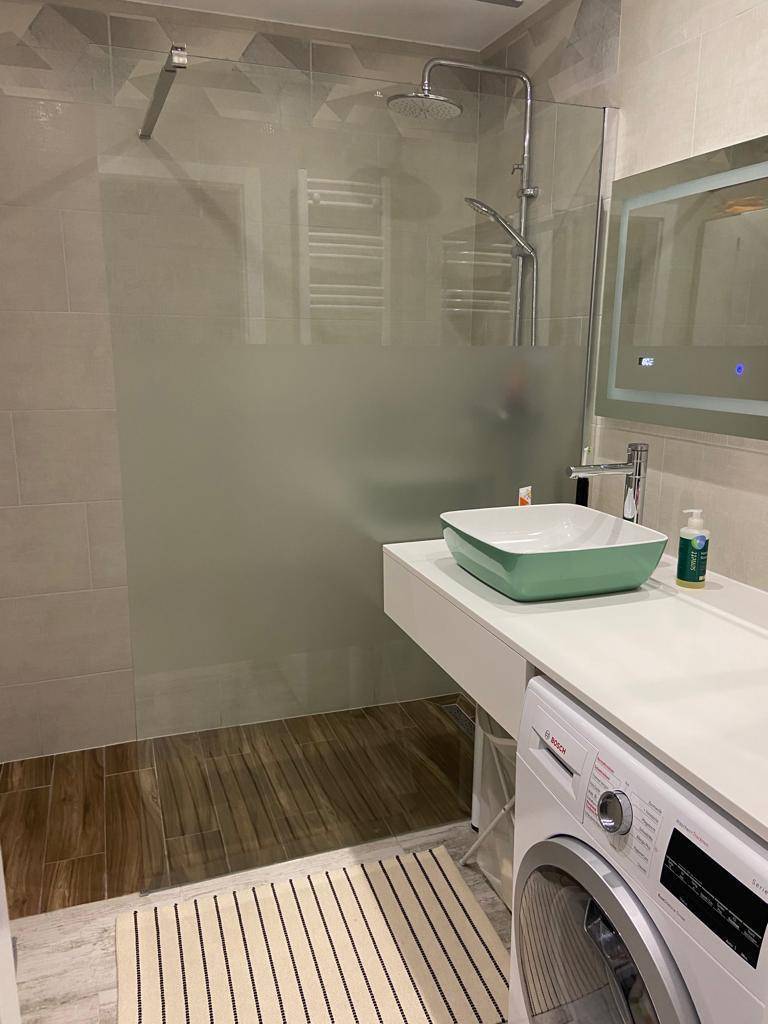 Helles Badezimmer mit großer begehbarer Dusche, Waschmaschine und modernem Waschbecken.
