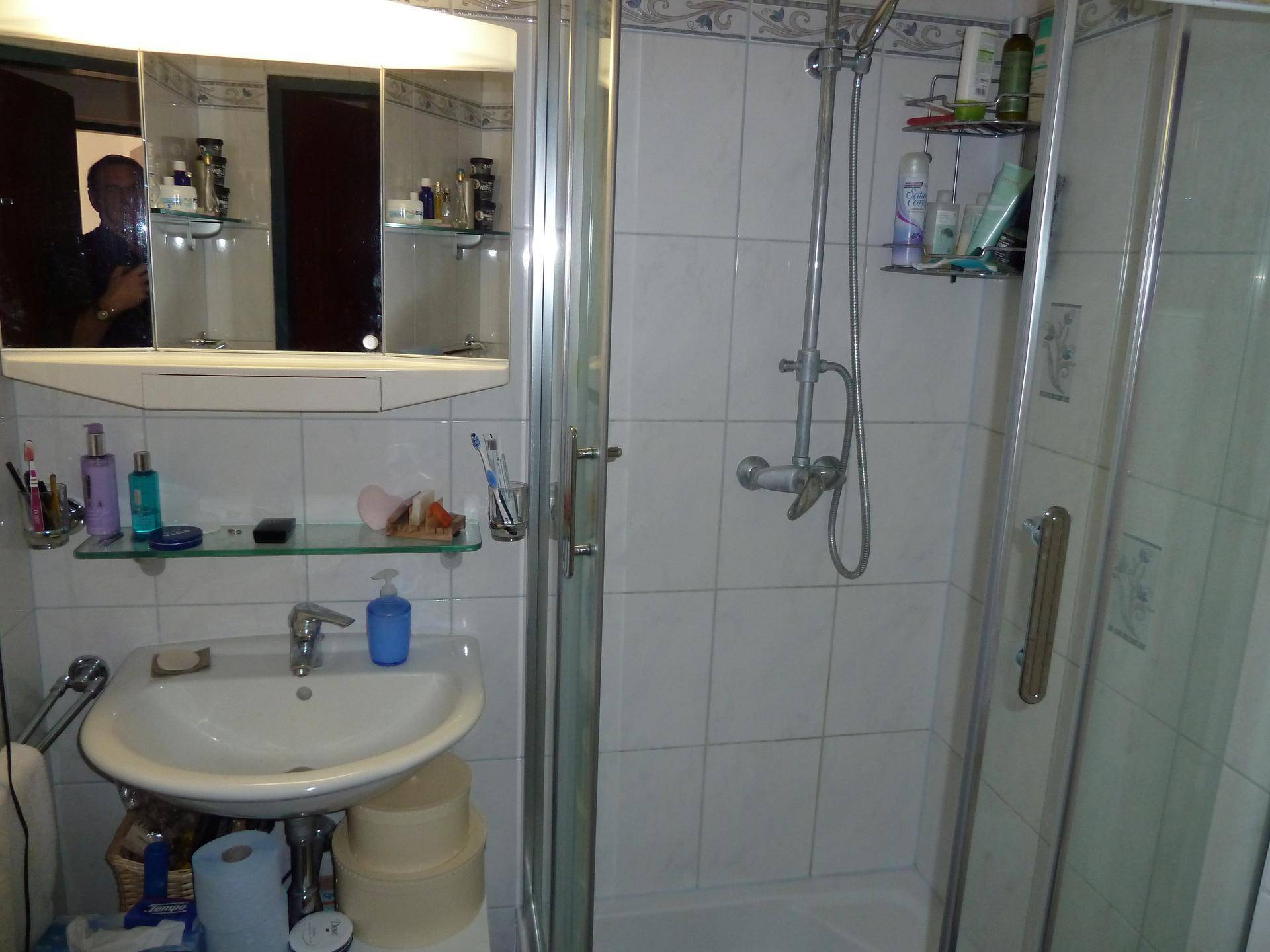 Helles Badezimmer mit Duschkabine, Waschbecken, Spiegelschrank und Fliesen an Wänden und Boden.