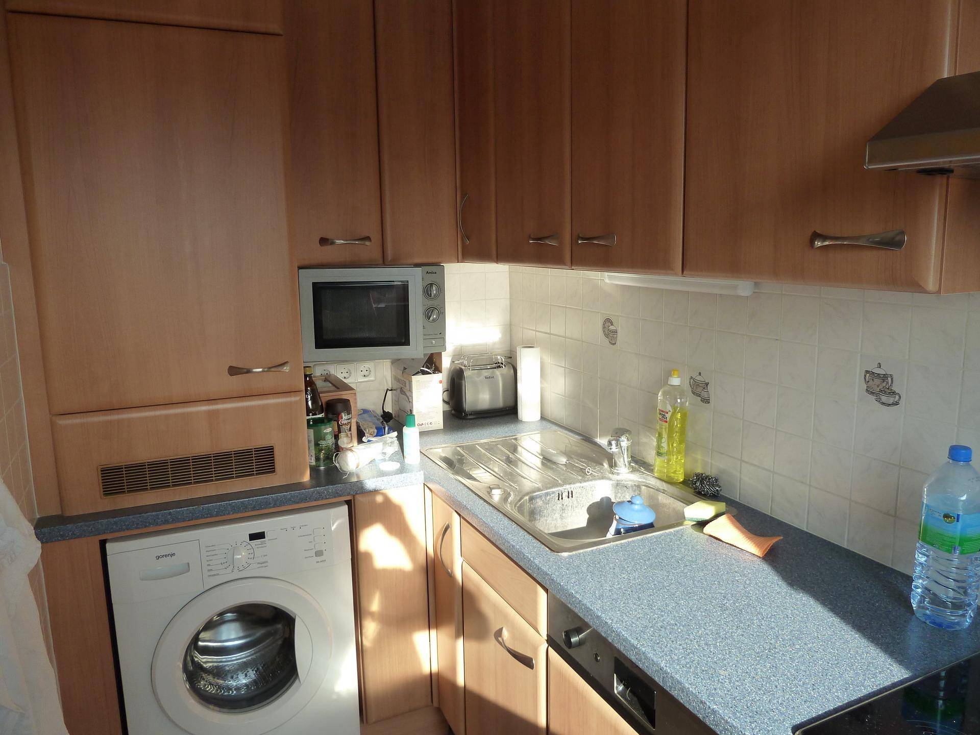 Küchenzeile mit Mikrowelle, Spülbecken und integrierter Waschmaschine unter Holzschränken.