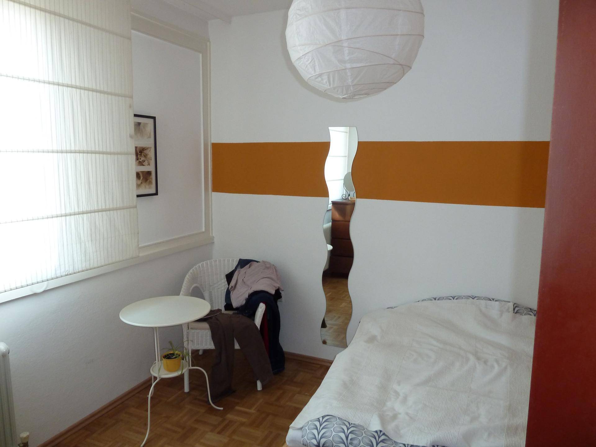 Gemütliches Schlafzimmer mit Einzelbett, Parkettboden und einem Fenster mit Jalousien.
