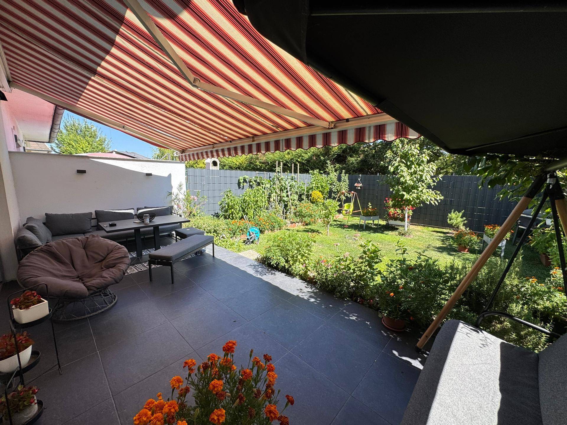 Große, geflieste Terrasse mit Markise, Gartenmöbeln und Blick auf den gepflegten Garten.