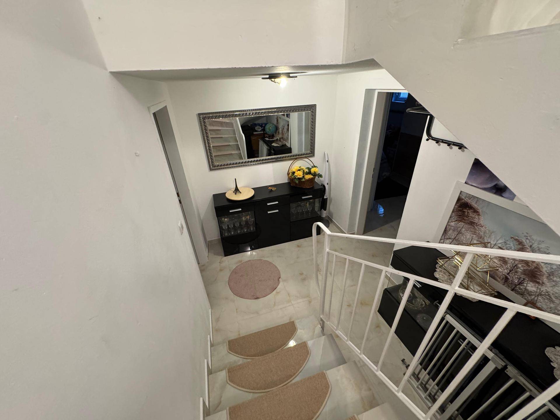 Blick von der Treppe in einen Flur mit Konsole, Spiegel und dekorativen Elementen.