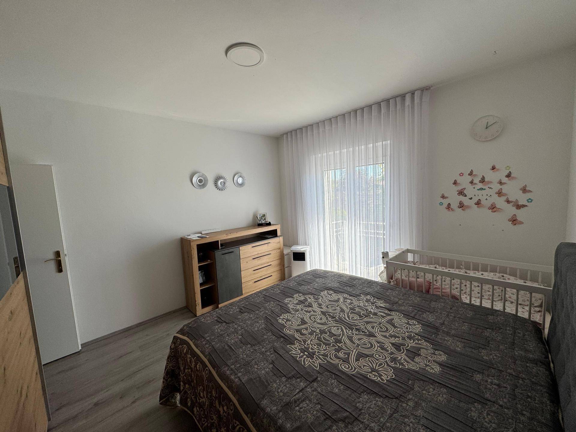 Schlafzimmer mit Kinderbett, Laminatboden und großen Fenstern, die viel Licht hereinlassen.